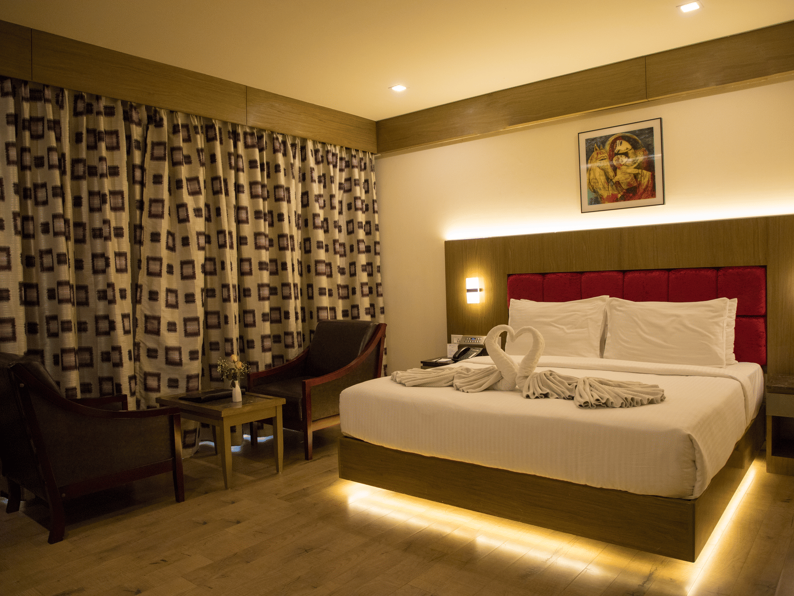 Full view of the Deluxe Room at the Benzz Park, Vellore, featuring a double bed with under-bed lights alongside a common seating area.