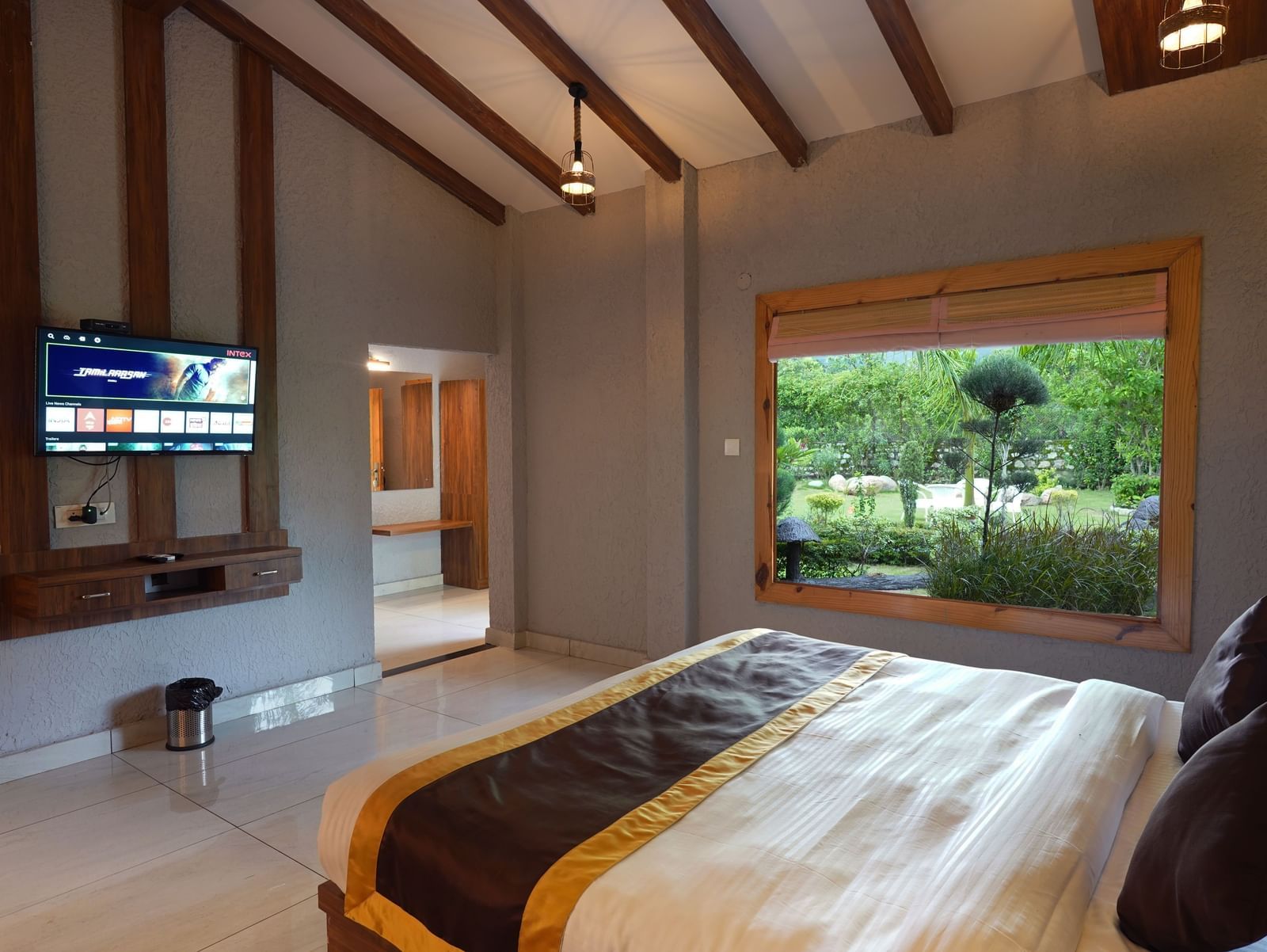 Spacious bedroom with wide window offering garden views at Corbett Nirvana Resort.