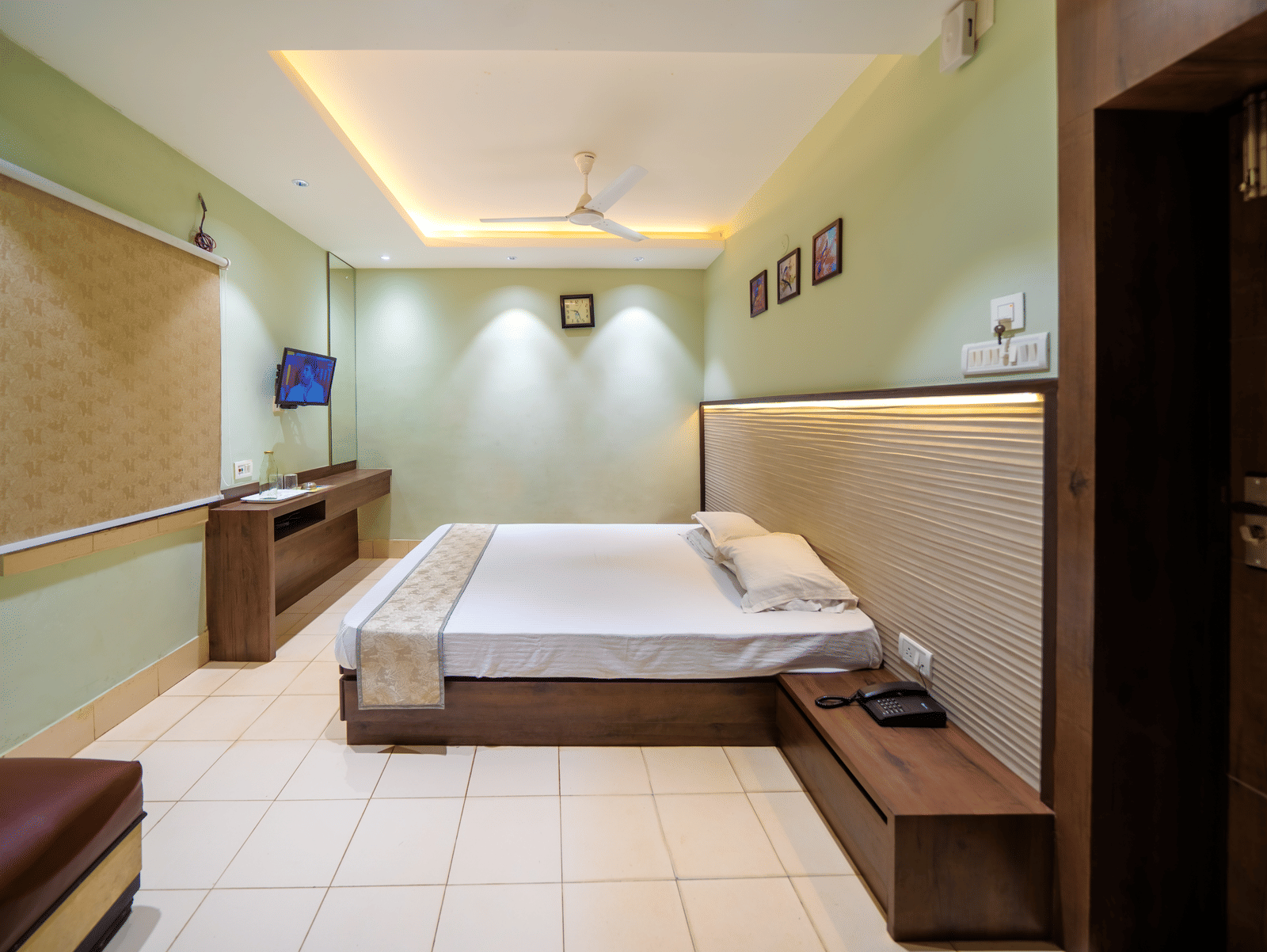Minimalist bedroom with a double bed, ceiling lights, wall-mounted TV, and light-coloured walls – Hotel Dolphin Puri