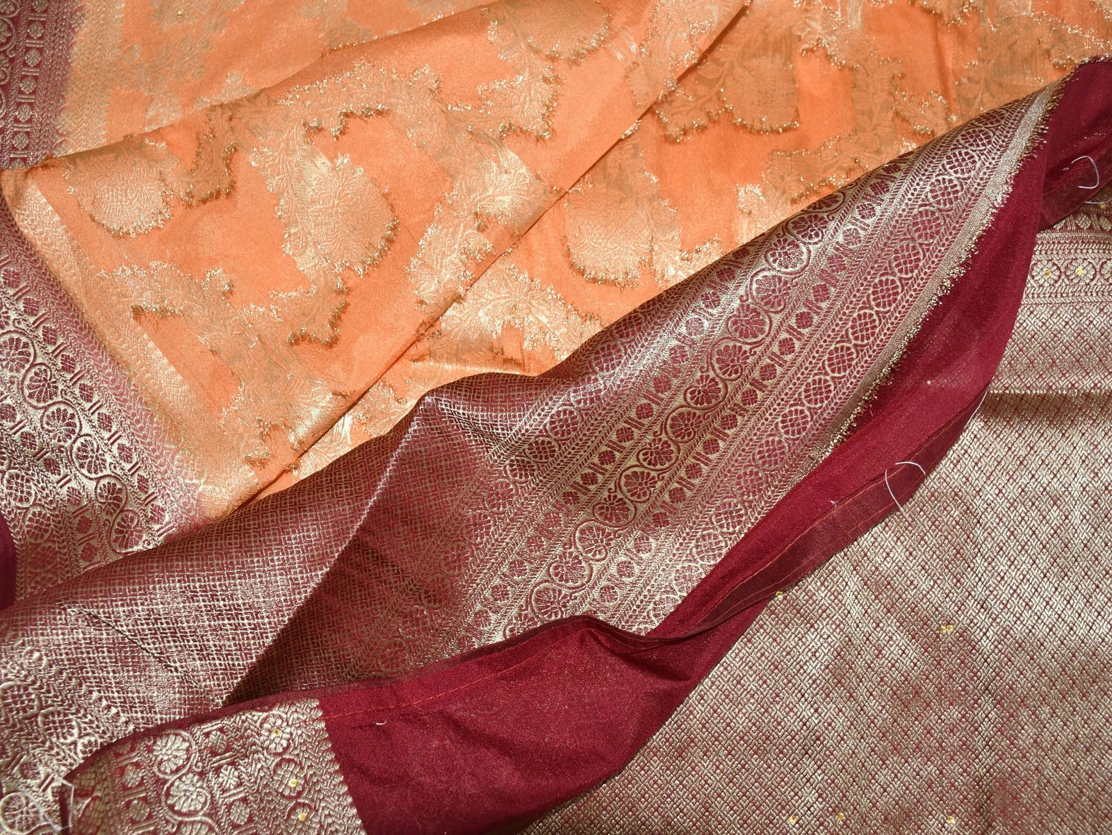 Folded fabric with intricate orange floral embroidery and maroon border.