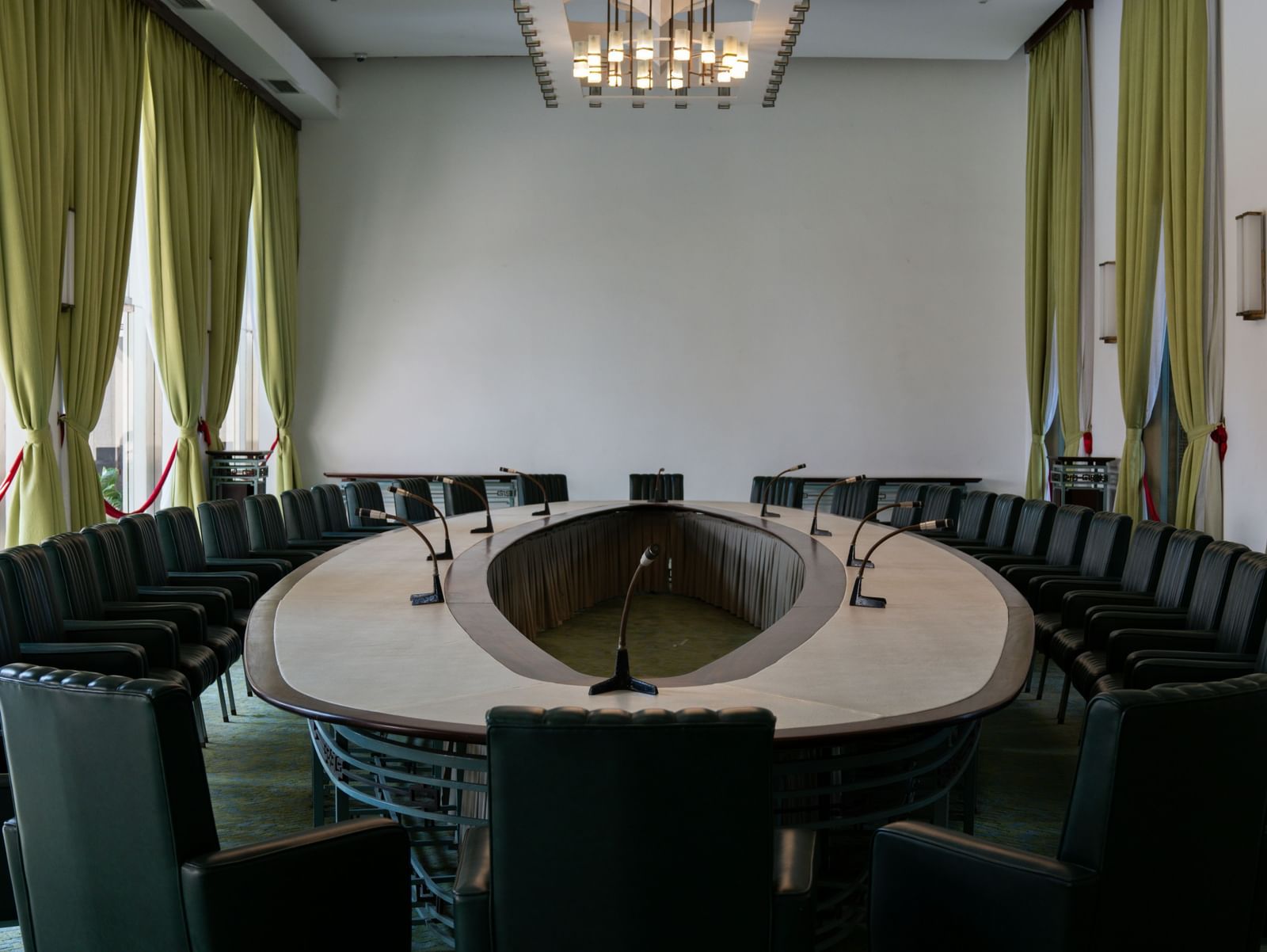 An elegant boardroom with a large round table, high-back chairs, and curtains on tall windows.