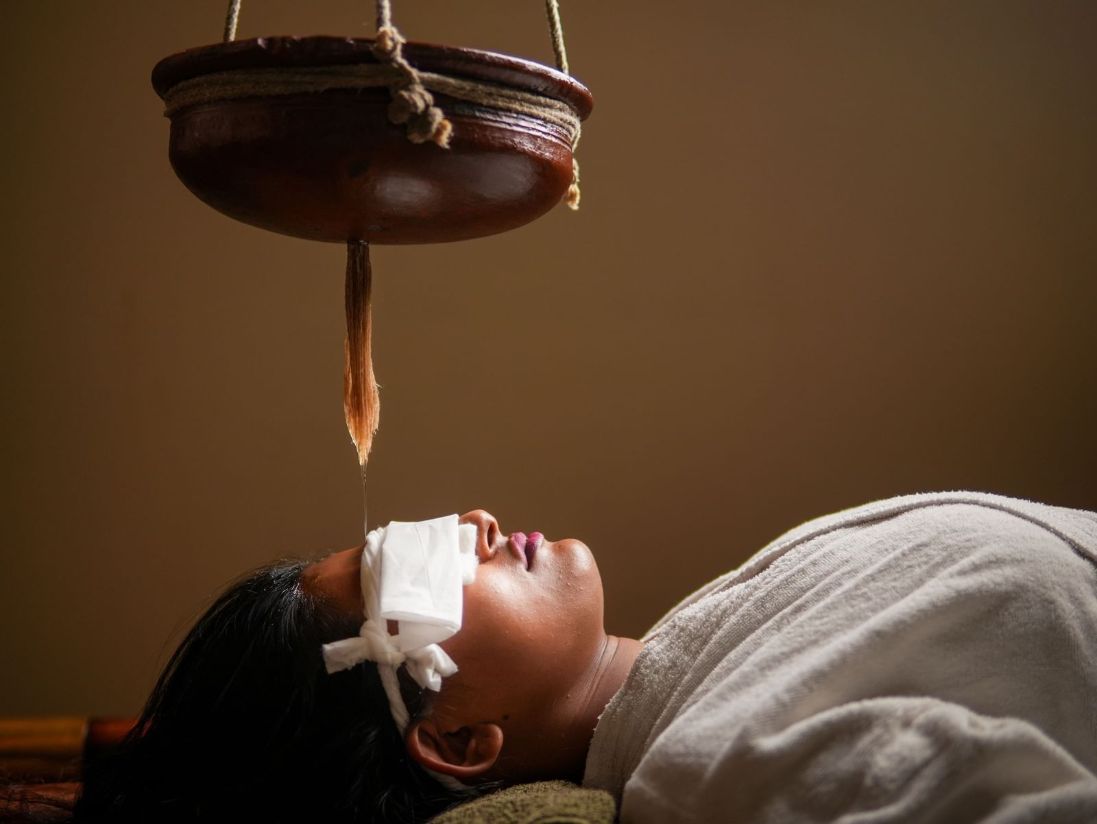 Shirodhara therapy in Vedic Village Spa Resort, featuring a stream of oil on a client's forehead.