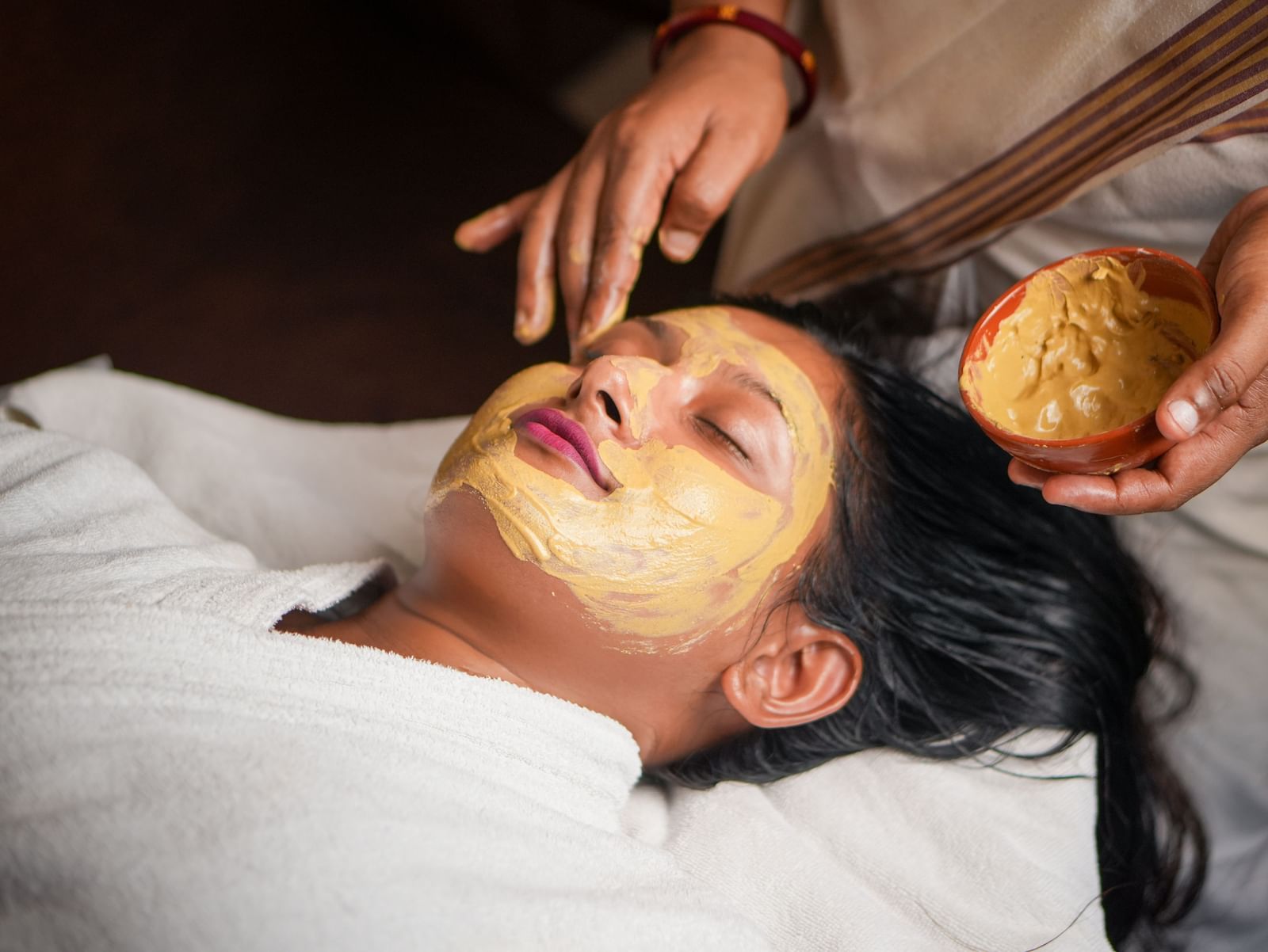 Facial mask application in Vedic Village Spa Resort, featuring a person receiving a natural face pack.
