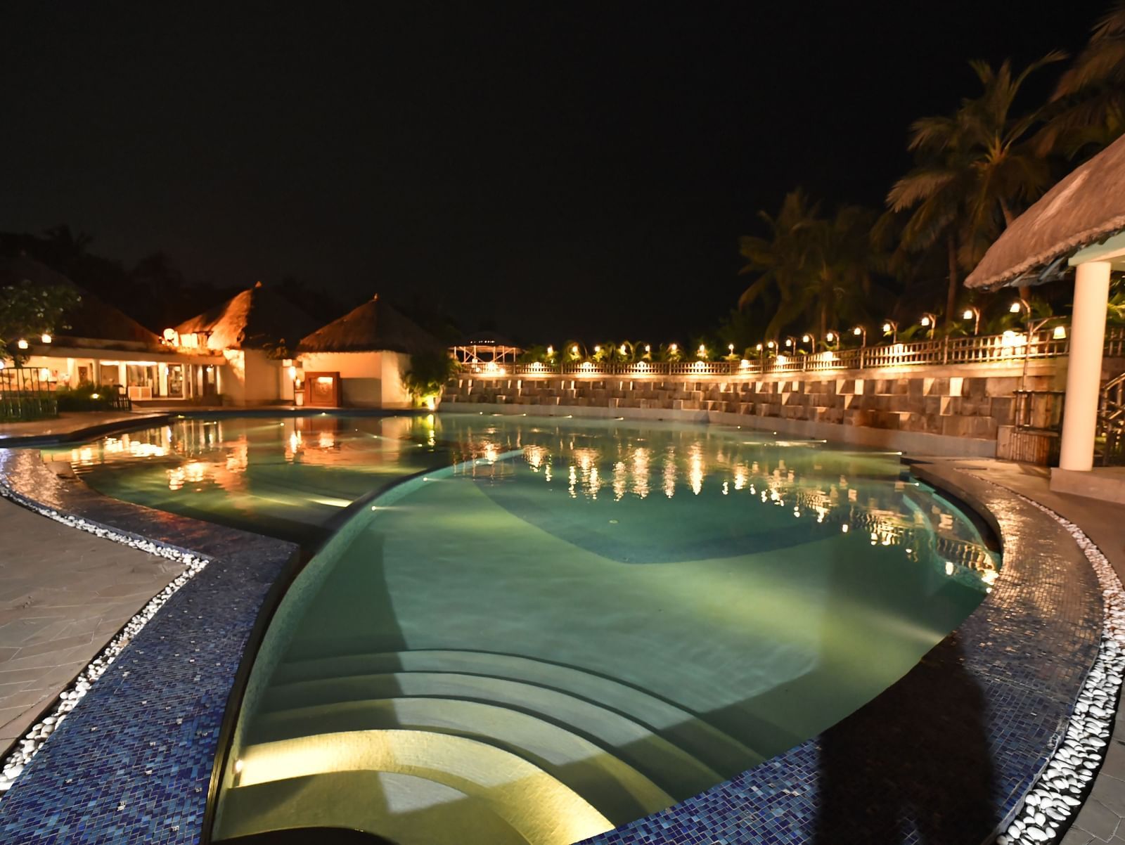 A swimming pool area is illuminated at night, surrounded by resort-style architecture