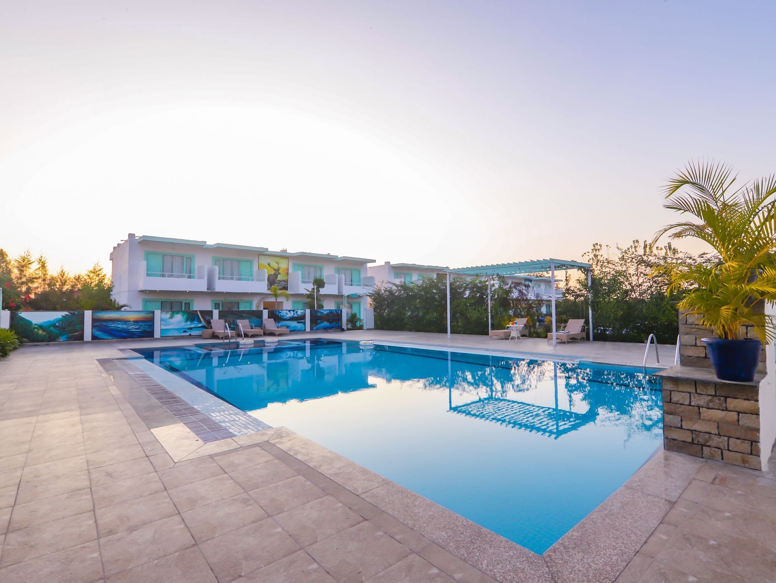 View of a swimming pool with buildings, trees and clear blue sky in the background - Vedikant Resorts The Mallard Corbett.