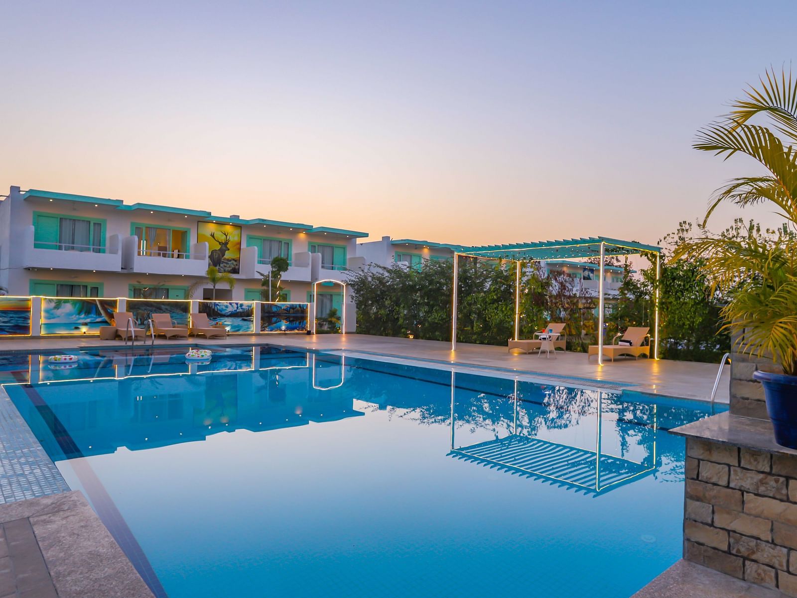 View of a swimming pool with trees, buildings and clear blue sky in the background - Vedikant Resorts The Mallard Corbett.