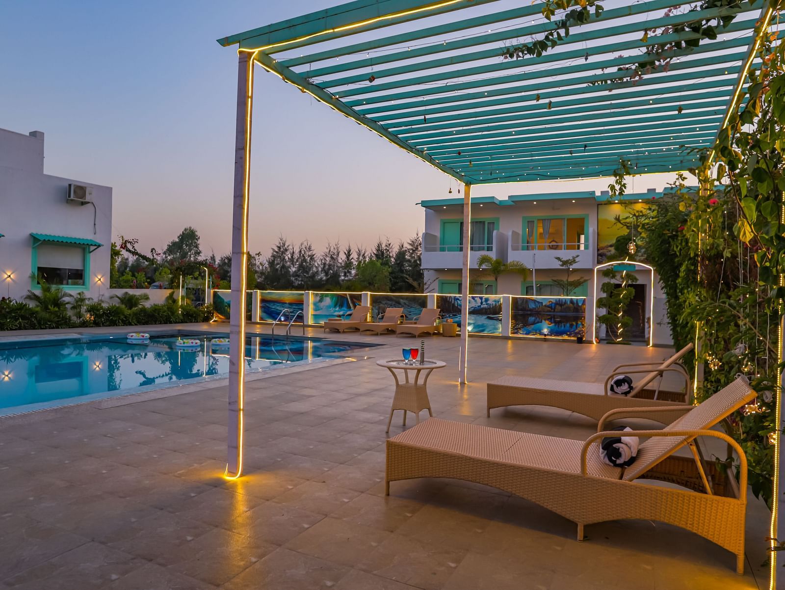 View of a swimming pool with sun lounger, trees, buildings and clear blue sky in the background - Vedikant Resorts The Mallard Corbett.