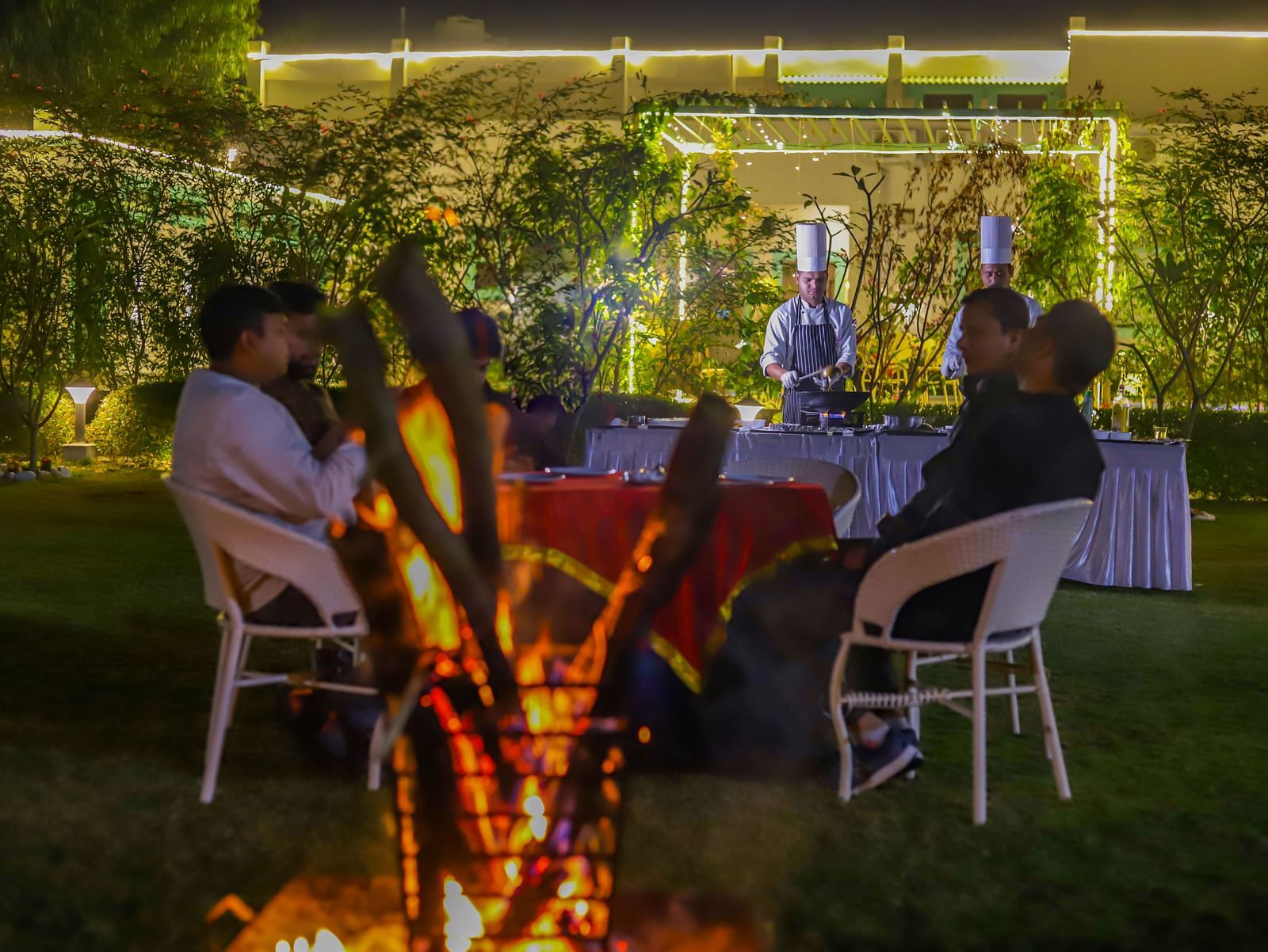Guests dine outdoors at Vedikant Resorts The Mallard Corbett with tables and chairs arranged on a lawn under decorative lighting.