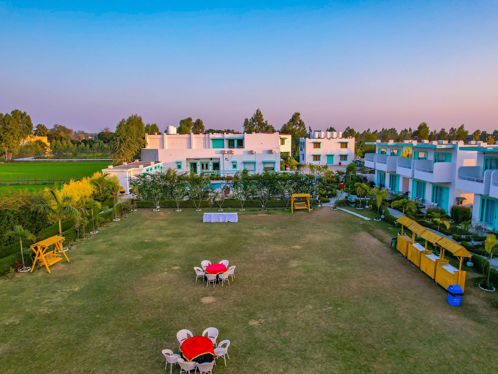 Lawn area at Vedikant Resorts The Mallard Corbett with tables and chairs set up outdoors, bordered by hedges and facing the rooms.