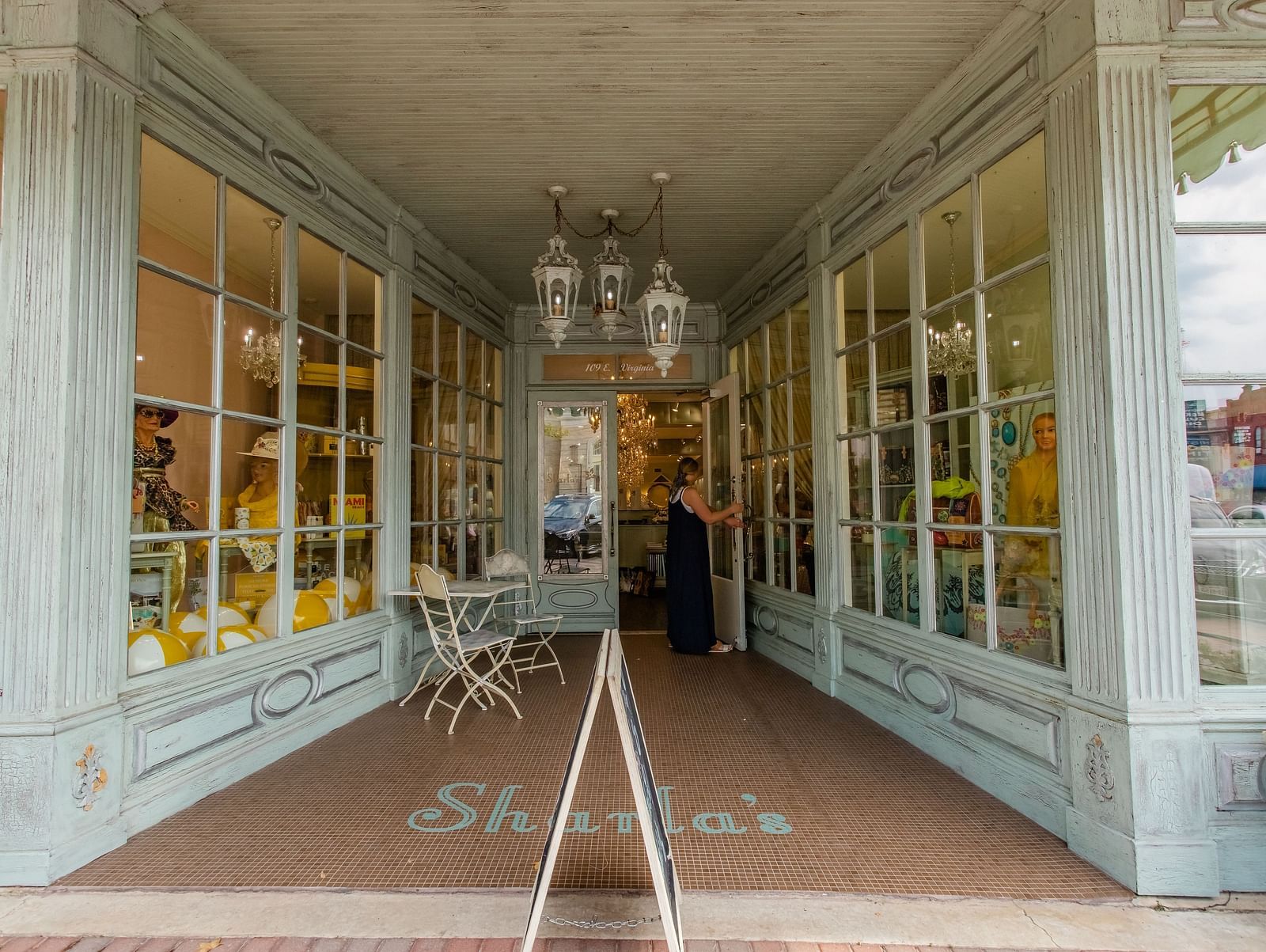 A boutique storefront with glass windows, a chandelier hanging in the entrance, and an elegant display inside.- The Grand Hotel & Ballroom, McKinney