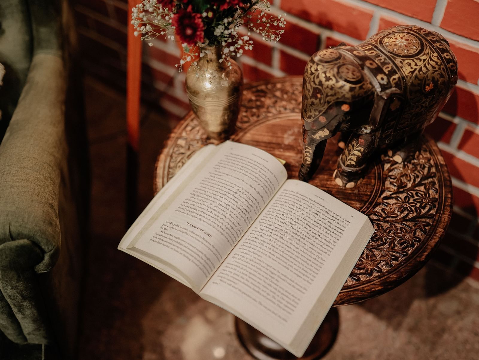 Open book on a small table with decorative items, with a glimpse of a green armchair  | Adhyaya Heritage Reverbed
