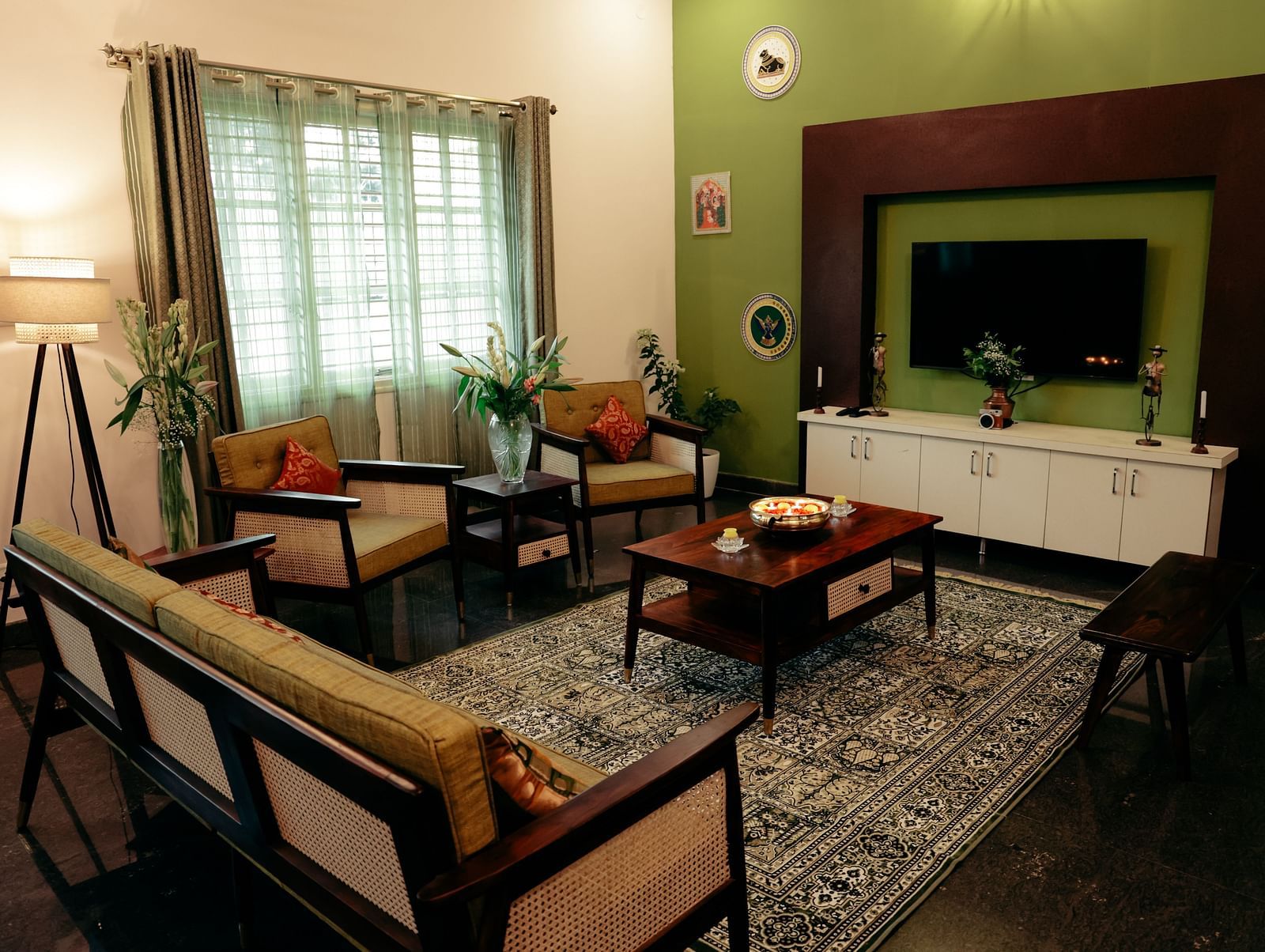 A living room with a green accent wall, a TV mounted on it, and a brown sofa set | Adhyaya Heritage Reverbed