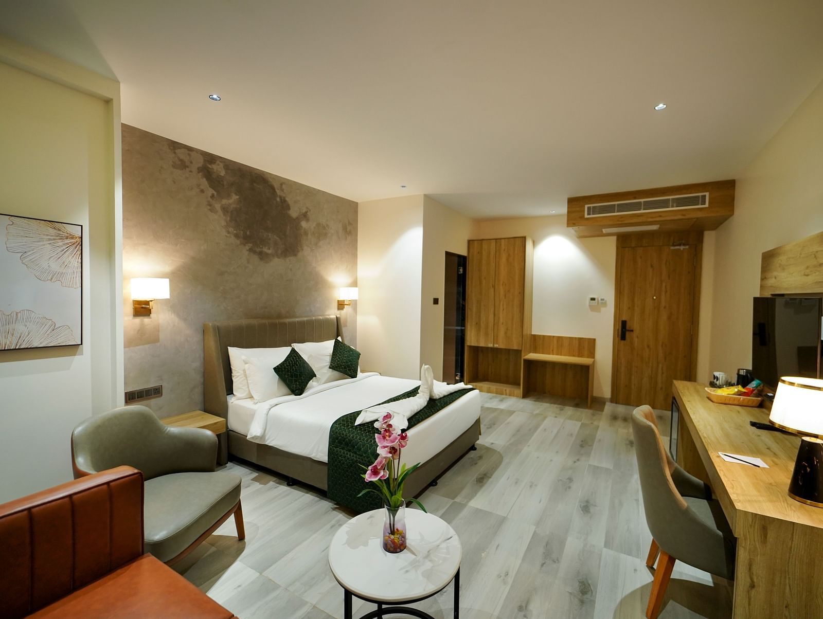A spacious hotel room includes a bed with pillows, a seating area with chairs and a small table with flowers, and a desk area - Hotel Park Inn, Nellore.