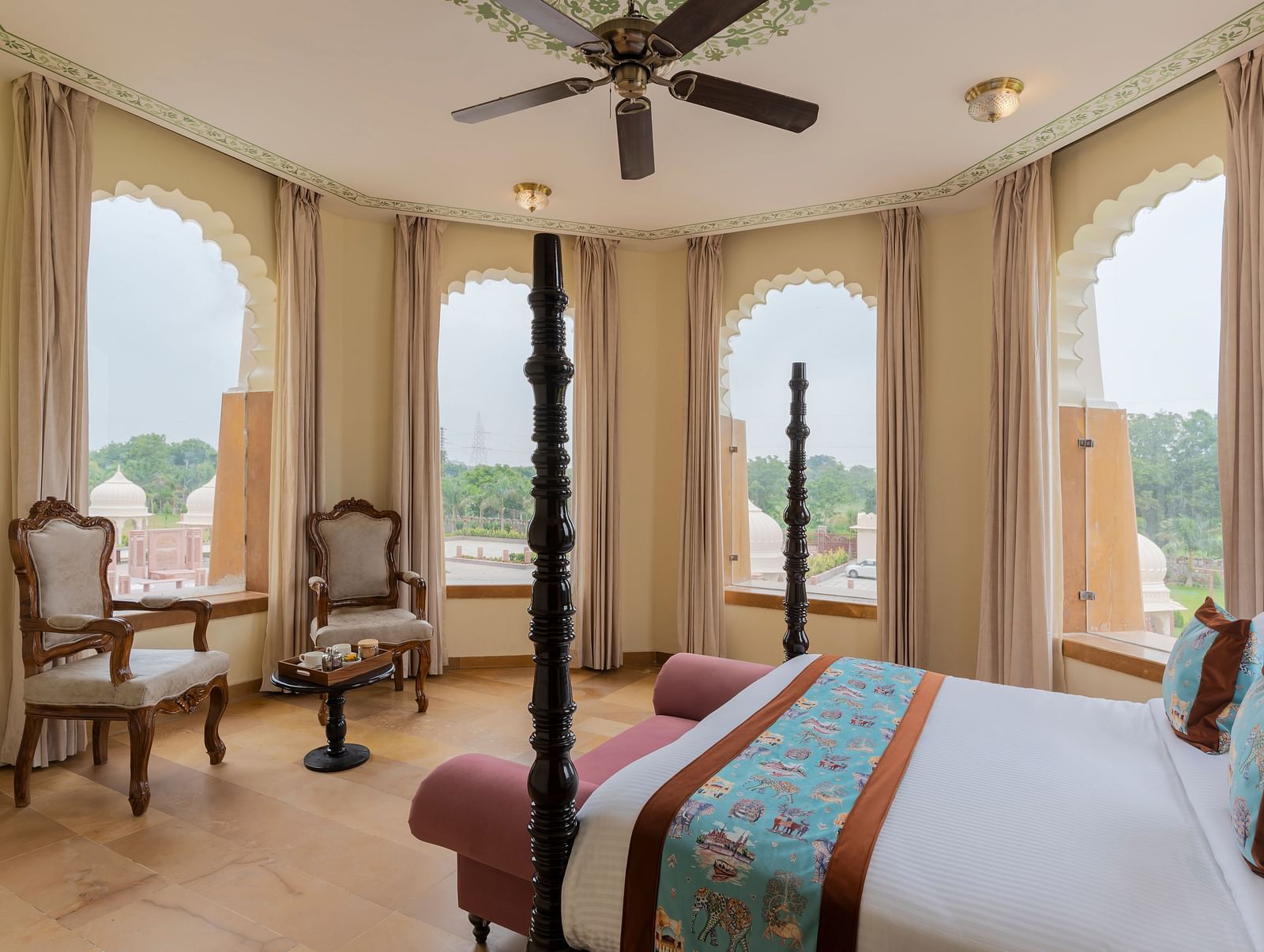 Elegant bedroom with arched windows overlooking scenic landscape at Kesar Bagh Palace.