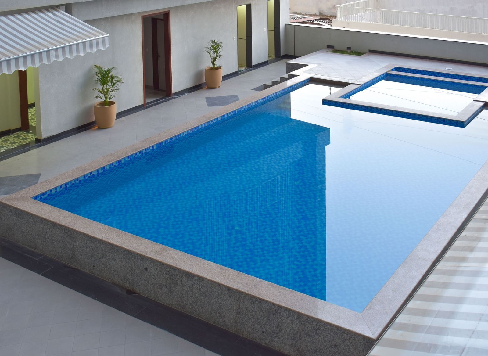 An outdoor swimming pool with blue tiles, surrounded by a concrete patio and potted plants - Urban Suites by BluSalzz, Jaipur