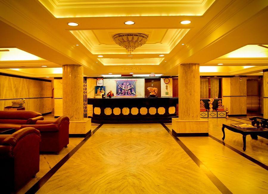 alt-text  Hotel Yasodha Towers - Interior view of the lobby area featuring supporting pillars and sofas in yellow lighting