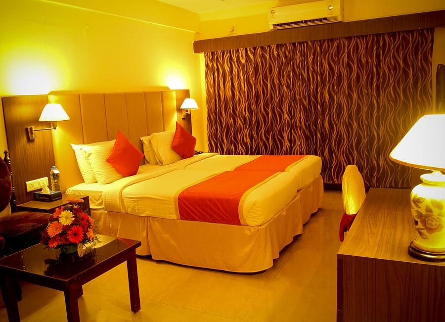 alt-text Hotel Yasodha Towers - Interior view of a bedroom containing a queen size bed illuminated with yellow coloured lamps 