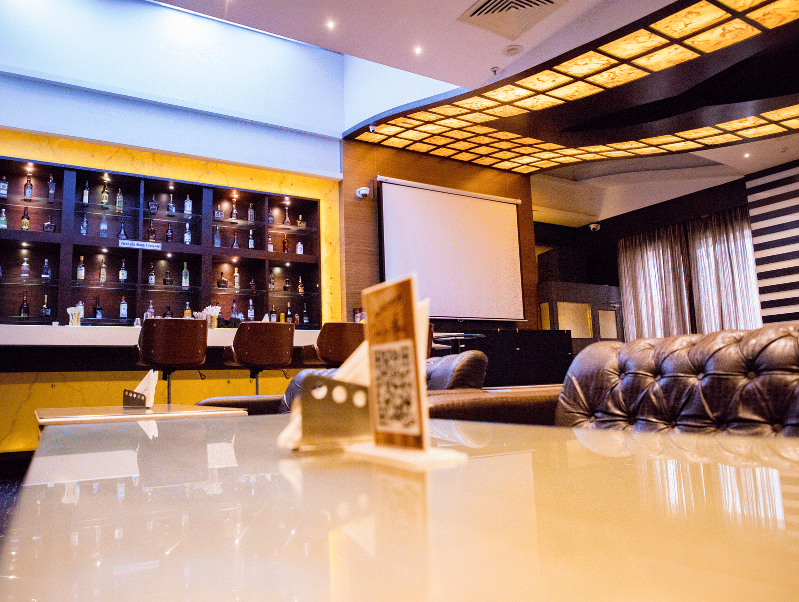 The bar at the Benzz Park, Vellore, taken from the dining table in the restaurant showcasing various liquor bottles on display behind the bar counter.