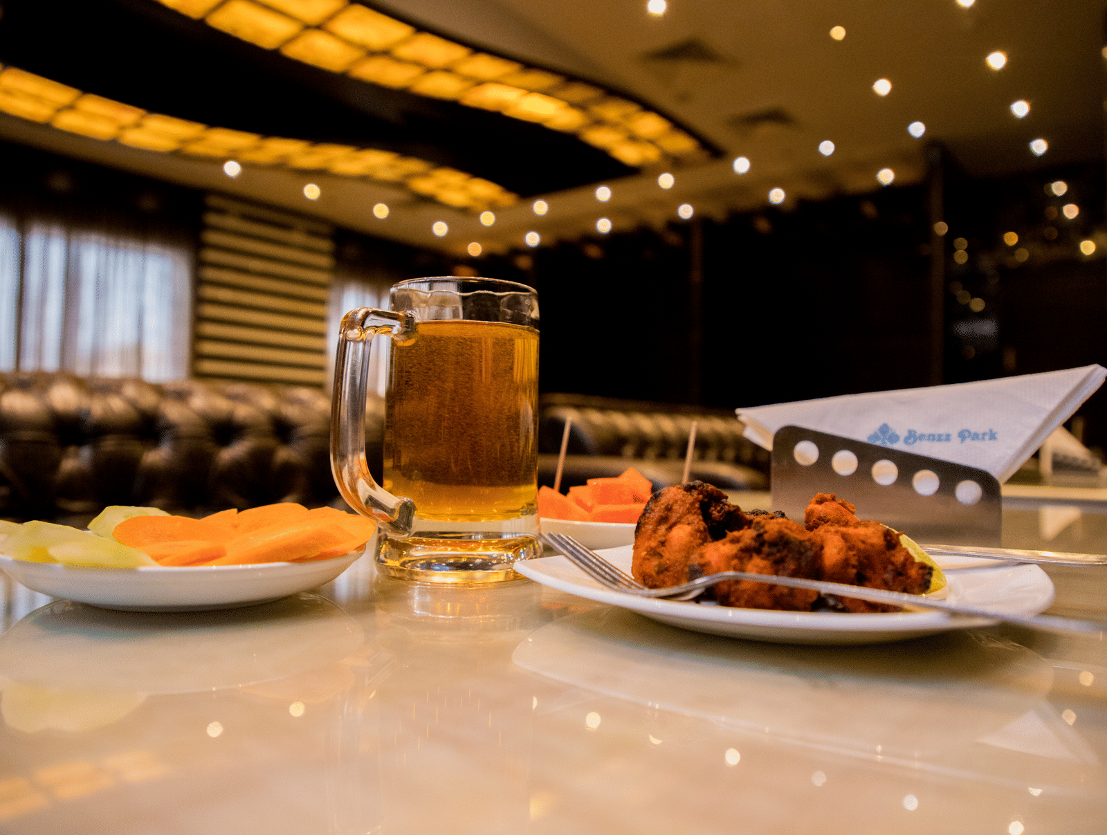 A close up shot of delicious side dish served with a plate of salad and a pint of beer on a dining table at Benzz Park, Vellore.