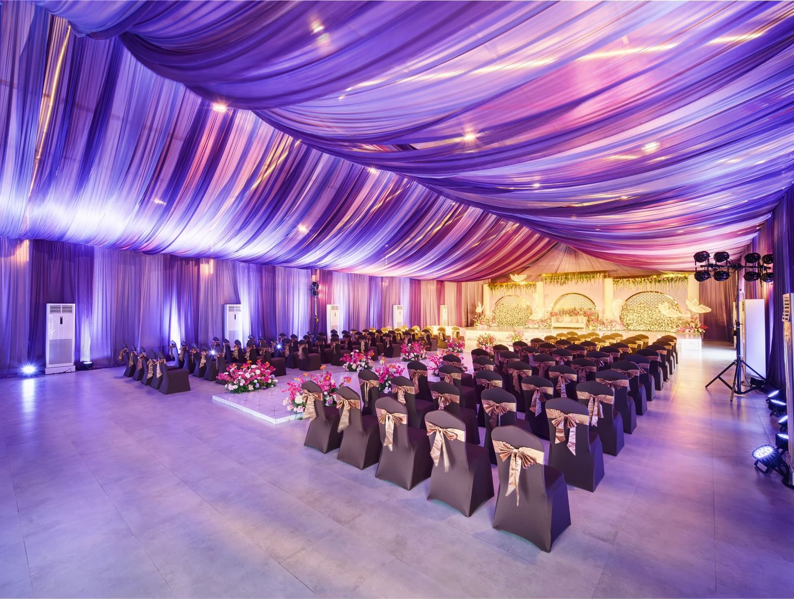 Decorated banquet hall with purple roof and rows of black chairs facing the stage at Grande Bay Resort & Spa.