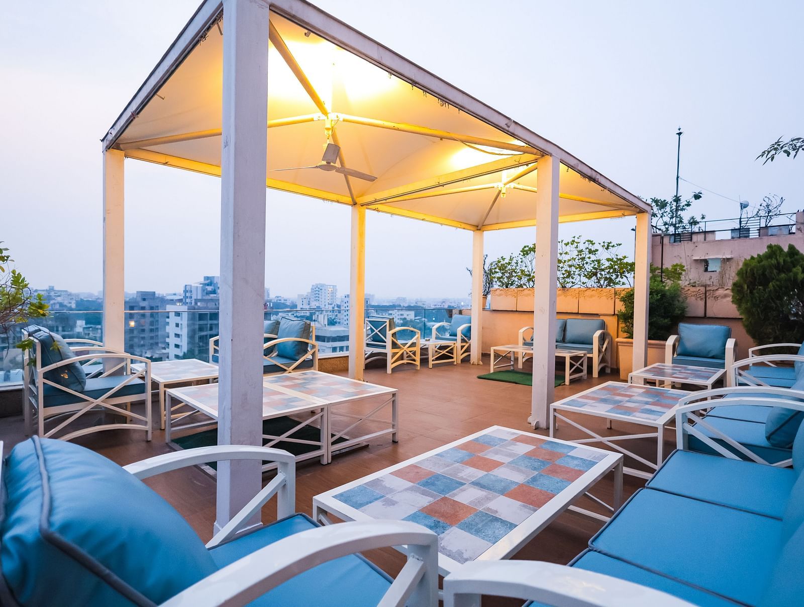 An outdoor dining setup at Hotel Ashok Nagpur featuring cushioned chairs and tables arranged on a rooftop or terrace during the evening.