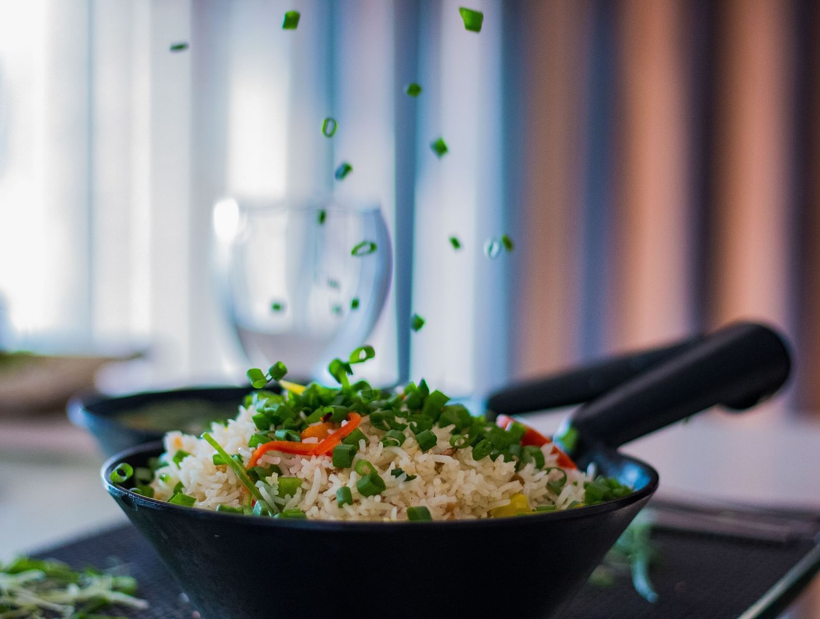 A black bowl filled with rice and green peas, with more peas being sprinkled from above.