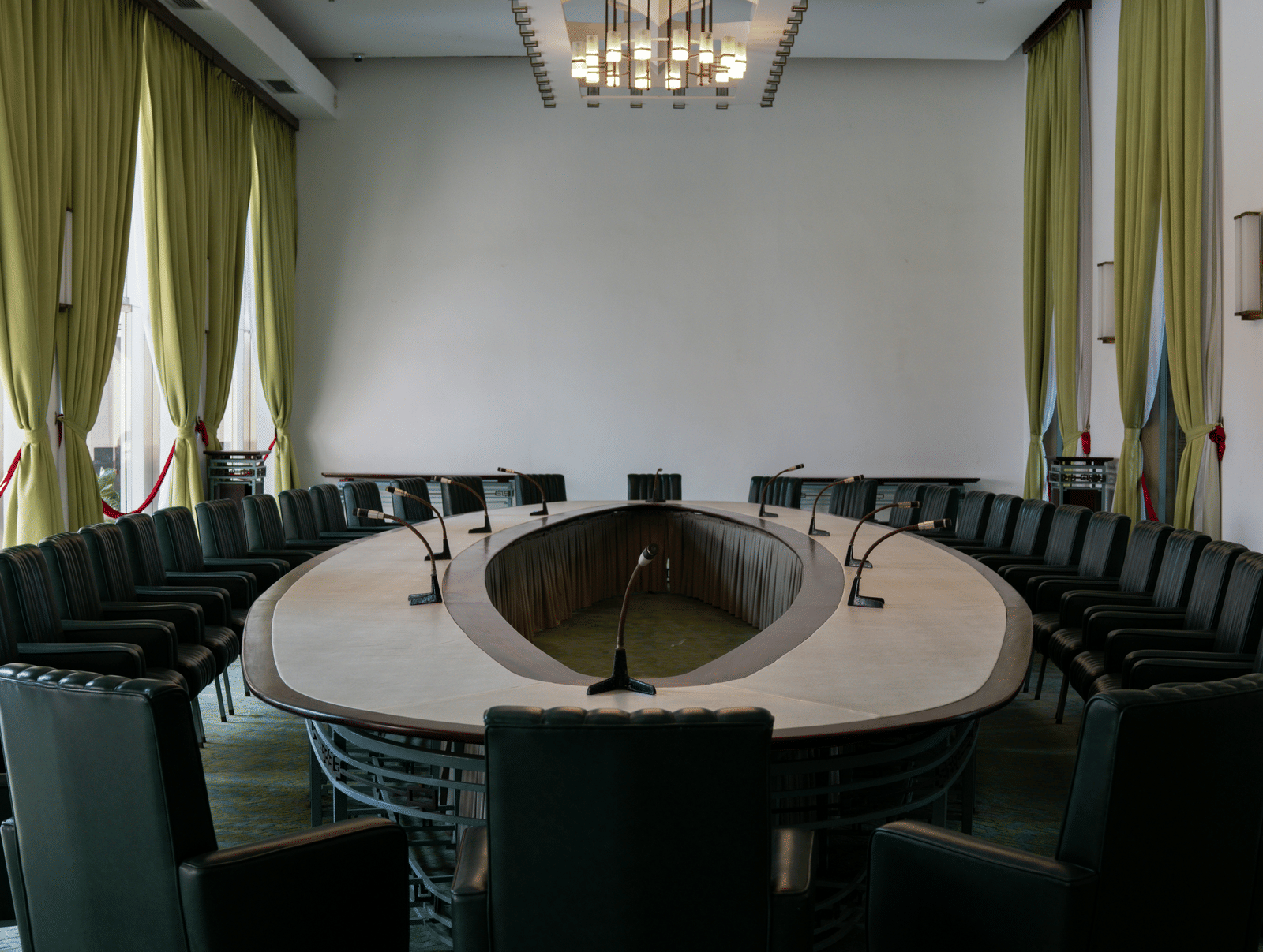 A conference room with round table, chairs, curtains, and a chandelier.