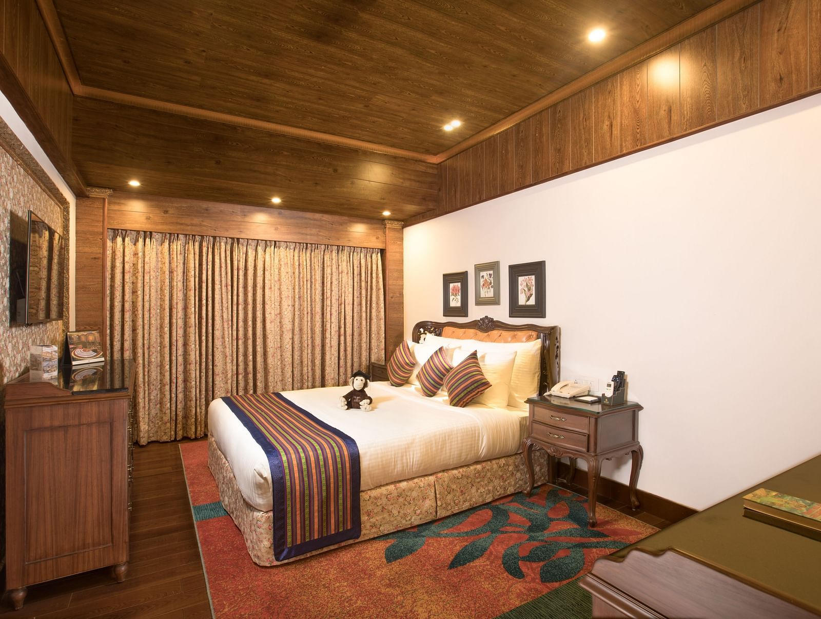 a plush bed facing the TV and the windows drapes closed - Mayfair Himalayan Spa Resort Kalimpong