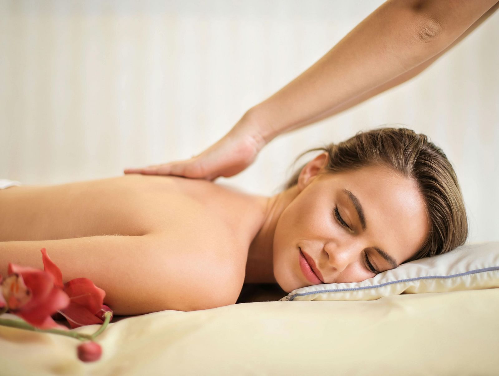 An woman lying on her stomach on a massage table getting a back massage with flowers placed beside her.