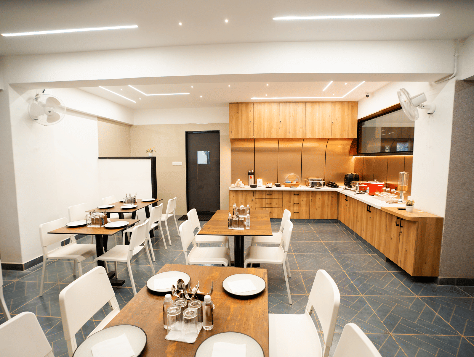 View of the restaurant with dining tables and chairs set, and a buffet counter in the background at Sunrise Business Hotel, Hyderabad.