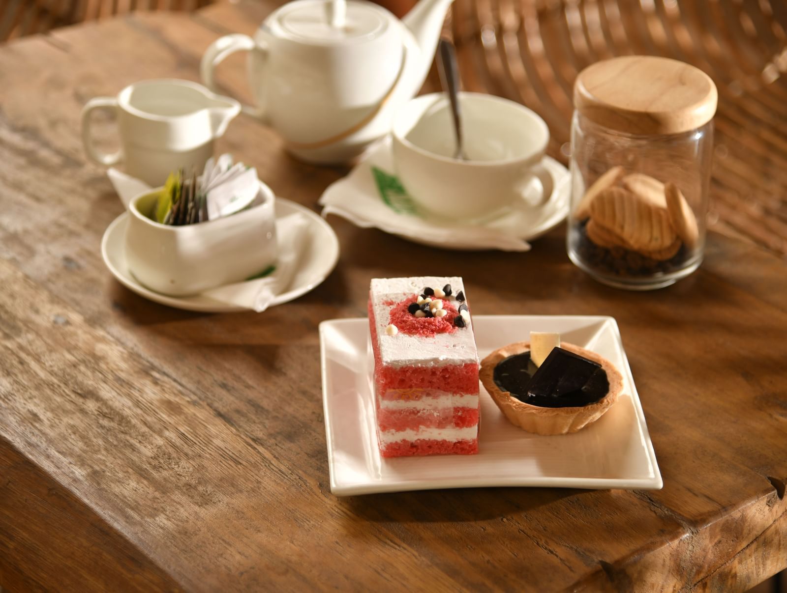 A tea set with cups, saucers, and a teapot is arranged on a table alongside a dessert | Chai