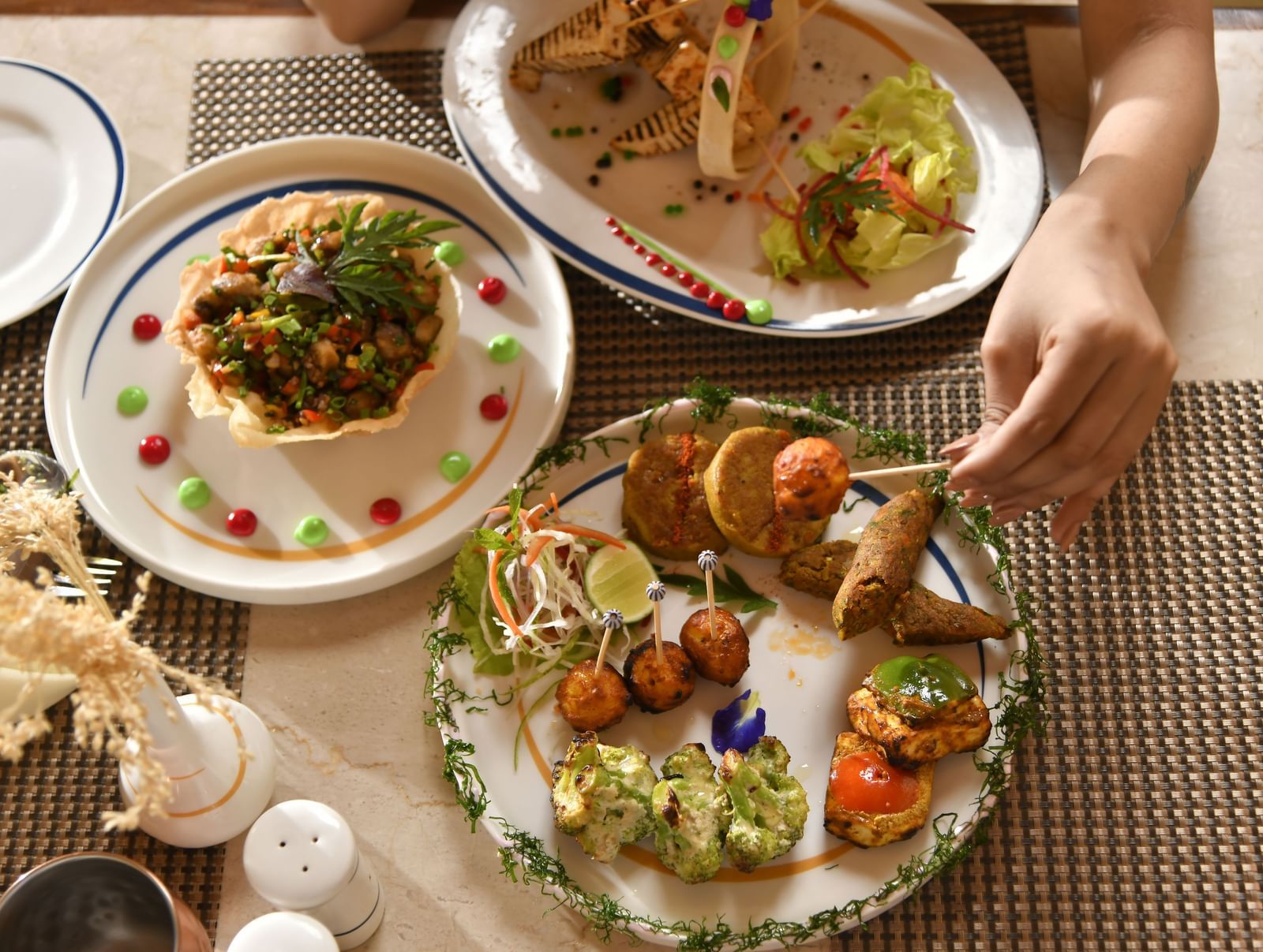 Hands are seen reaching for food served on plates, indicating a meal | Yagna
