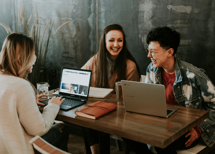 Three people sitting around a table laughing and working together on laptops at a cafe
