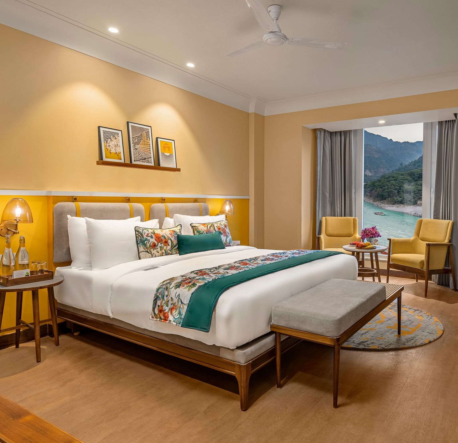  The room features a king-size bed with a plush headboard and comofrtable bedding. Armchairs by the window, offering a scenic view of the mountains. The room also includes a wooden desk, a television, and a ceiling fan. 
