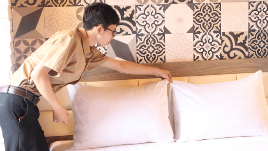 Hotel staff arranging pillows on a bed