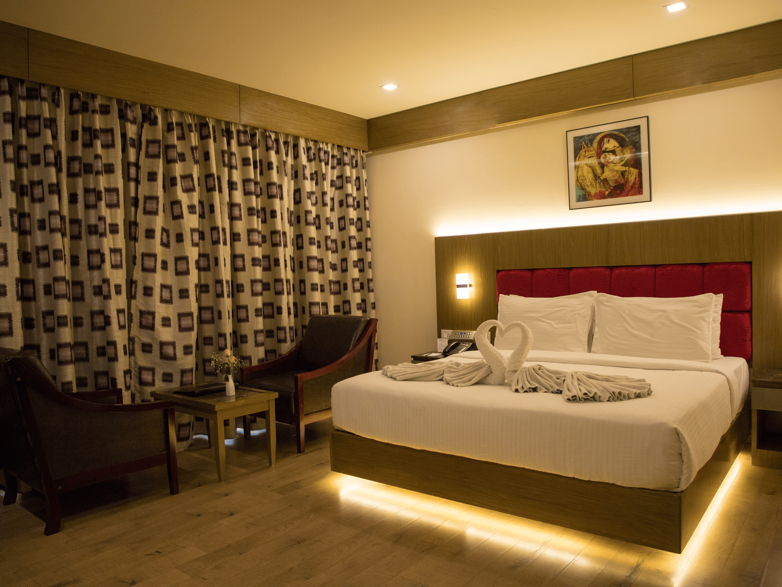 Full view of the Deluxe Room at the Benzz Park, Vellore, featuring a double bed with under-bed lights alongside a common seating area.