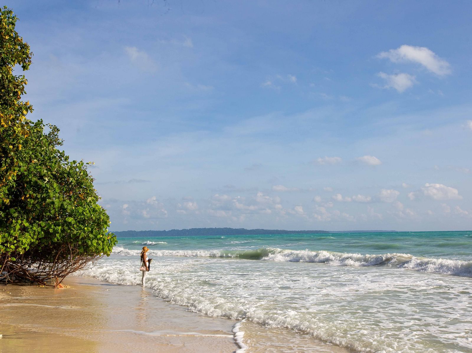 A wide, open beach with soft waves lapping at the shore. A person is walking along the water’s edge, enjoying the tranquil atmosphere - Coral Reef Resort & Spa, Havelock