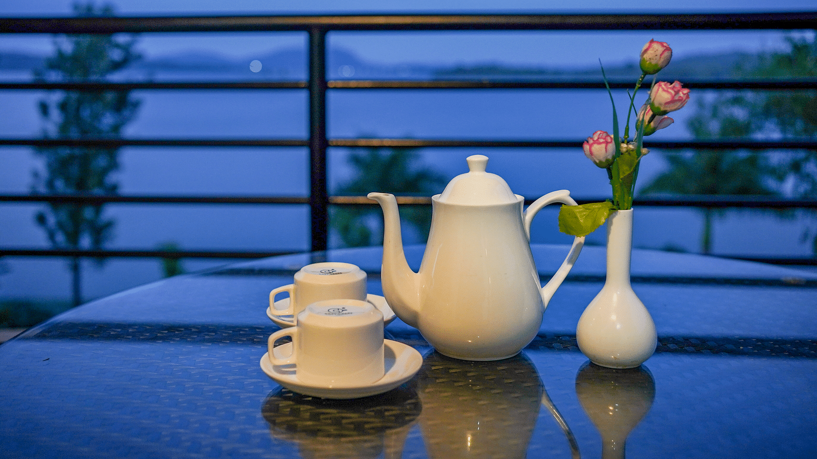 Image of a teapot and two cups placed on a table alongside a vase of flowers at Coorg Jungle Camp Backwater Resort, Kushalnagar.