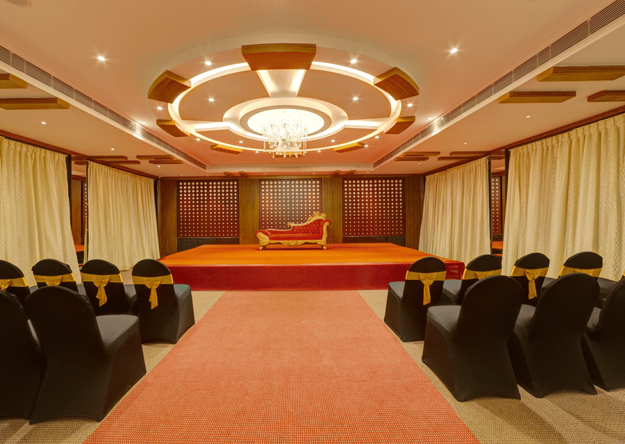 Rows of black chairs, a central red carpet, and a small stage in the event hall at Icon Express By Bhagini, Mahadevapura.