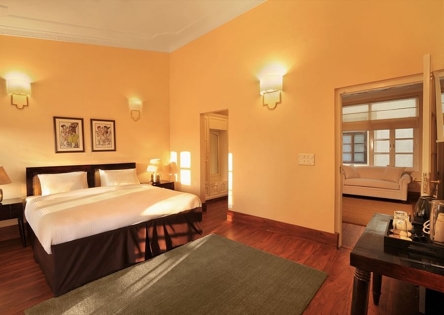 An image of a Super Deluxe room with a double size bed, bedside table with lamps on either side, and a table where antique and decorative items are placed - Lamrin Boutique Cottages Rishikesh