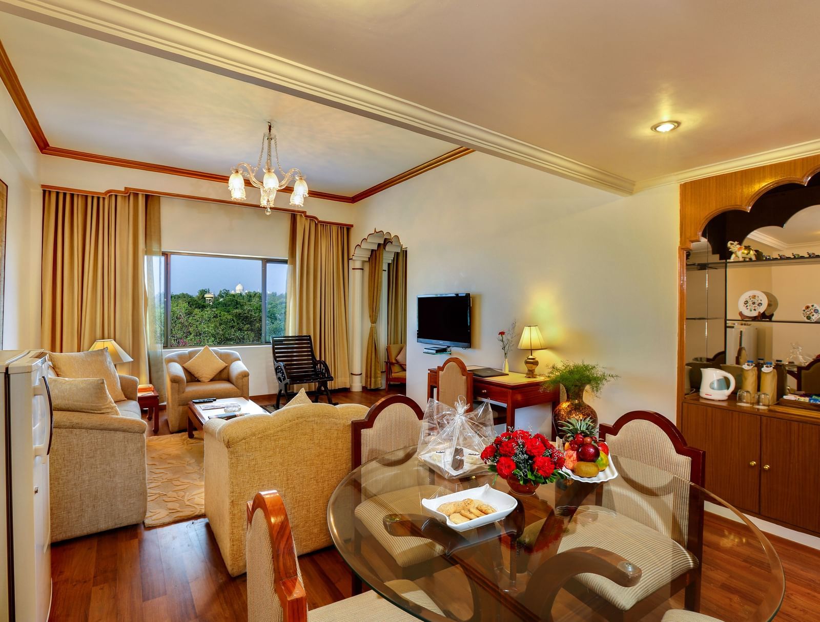 A well-lit living area of a room near Taj Mahal at Clarks Shiraz, Agra, featuring sofas, dining area, a wall-mounted TV, and wooden furnishings.