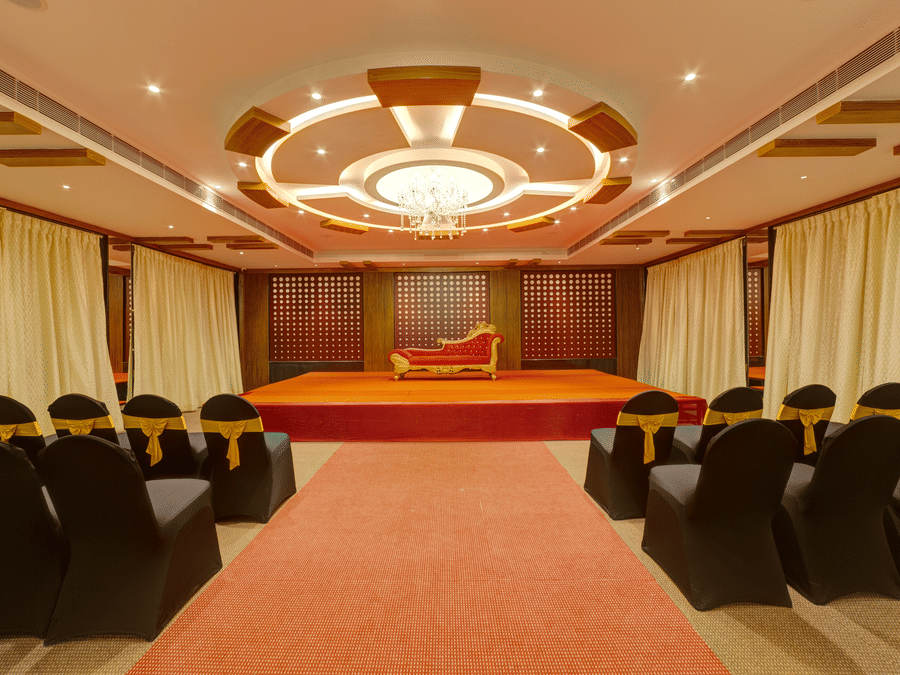 Rows of black chairs, a central red carpet, and a small stage in the event hall at Icon Express By Bhagini, Mahadevapura.