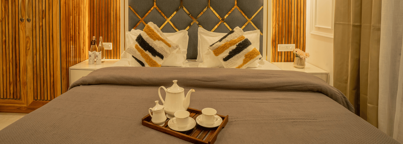 A bedroom with a king size bed, 2 bedside tables, a wardrobe, and a tray with a teapot and cups on the bed at Perfectstayz Value Paradise, Mussoorie.