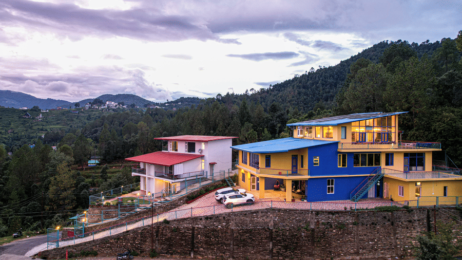 An aerial view of  Adrushya Estates, a luxury resort in Mukteshwar, with buildings, pathways, and surrounding mountains under a cloudy sky