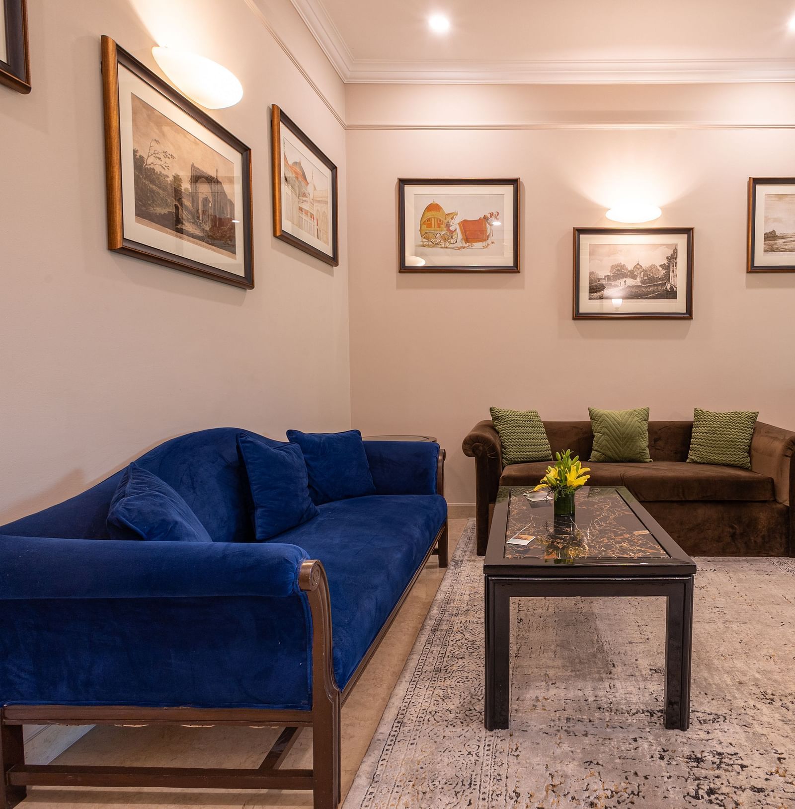 Corner view of the Grand Luxury Twin Bed Room at The Claridges New Delhi, featuring a cosy sofa with a table in front and framed photos on the wall