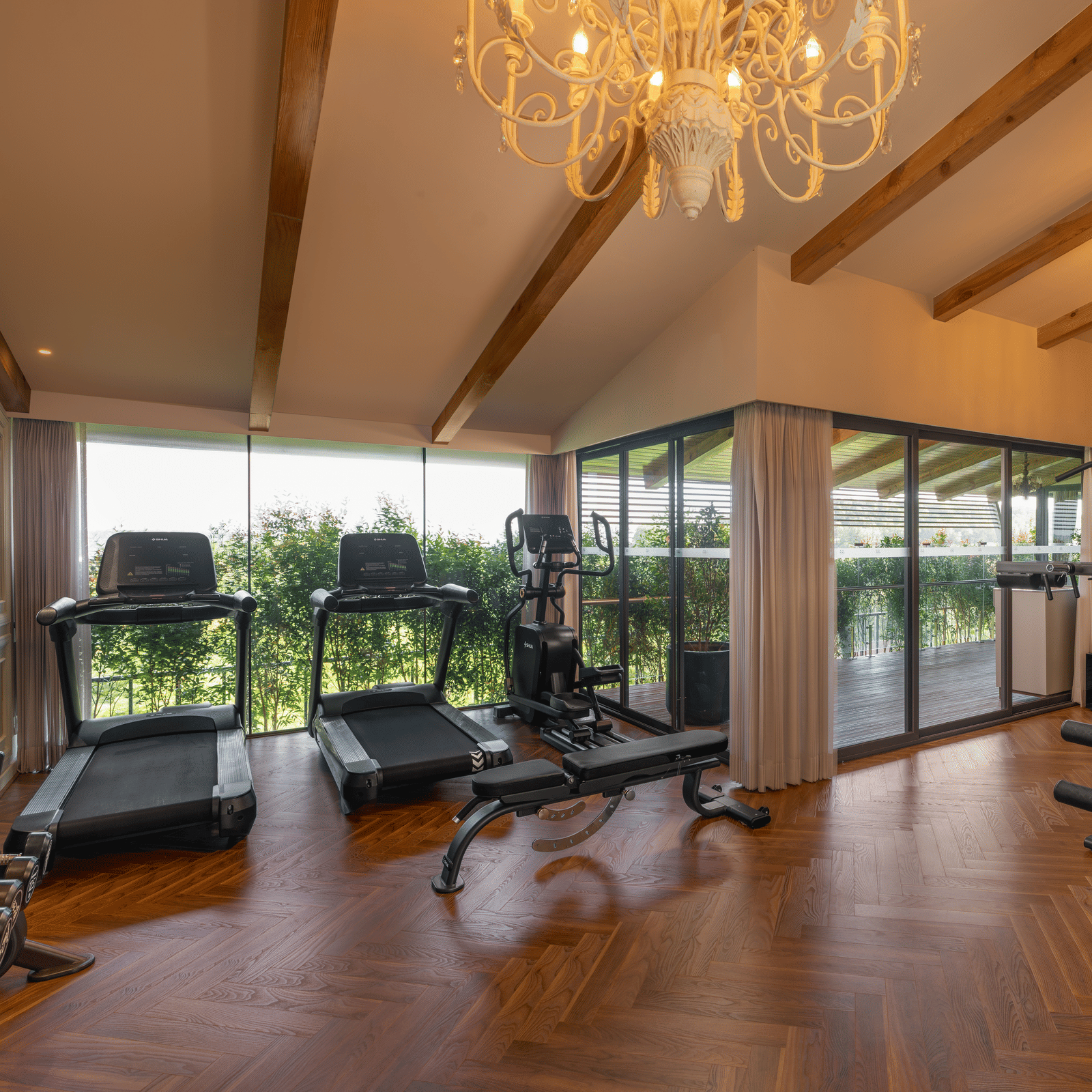 A wide-angle shot of the full-equipped gym at The Evren, Vagator, featuring elegant chandeliers hanging from the ceiling.