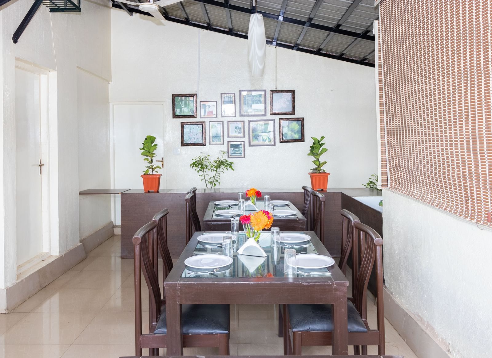 A dining area with a wooden table, chairs, and decorated with framed pictures and potted plants at Sanctum Suites Domlur, Bangalore.