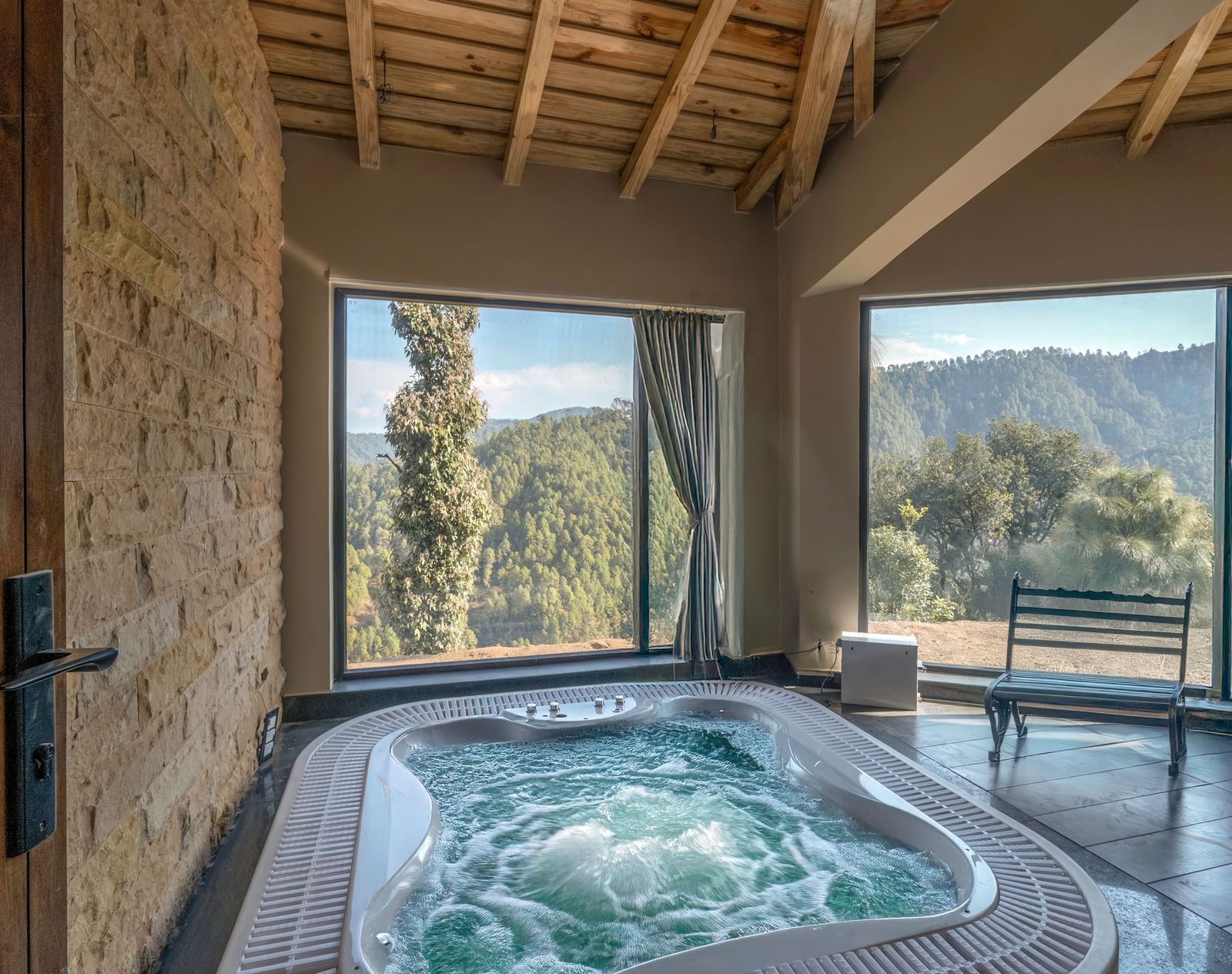 Spacious room with a Jacuzzi placed beside the wall and a seating area to the side, next to large windows with curtains pulled to the side at The Chamomile Estate.