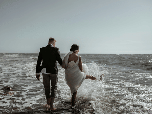 Couple holding hands while walking along the beach during a moody sunset