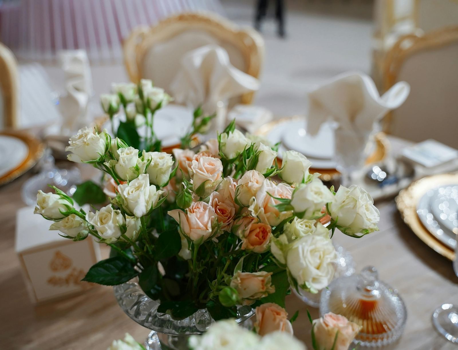 A close up shot of a beautiful flower vase with a lot of white and pink roses on a dining table.